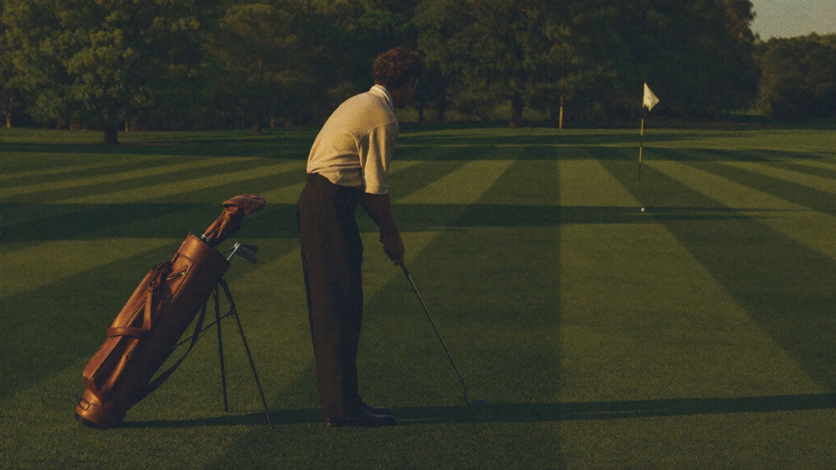 A gentleman golfer in classic attire lining up at a target flag on an old-money driving range, vintage leather golf bag at his side