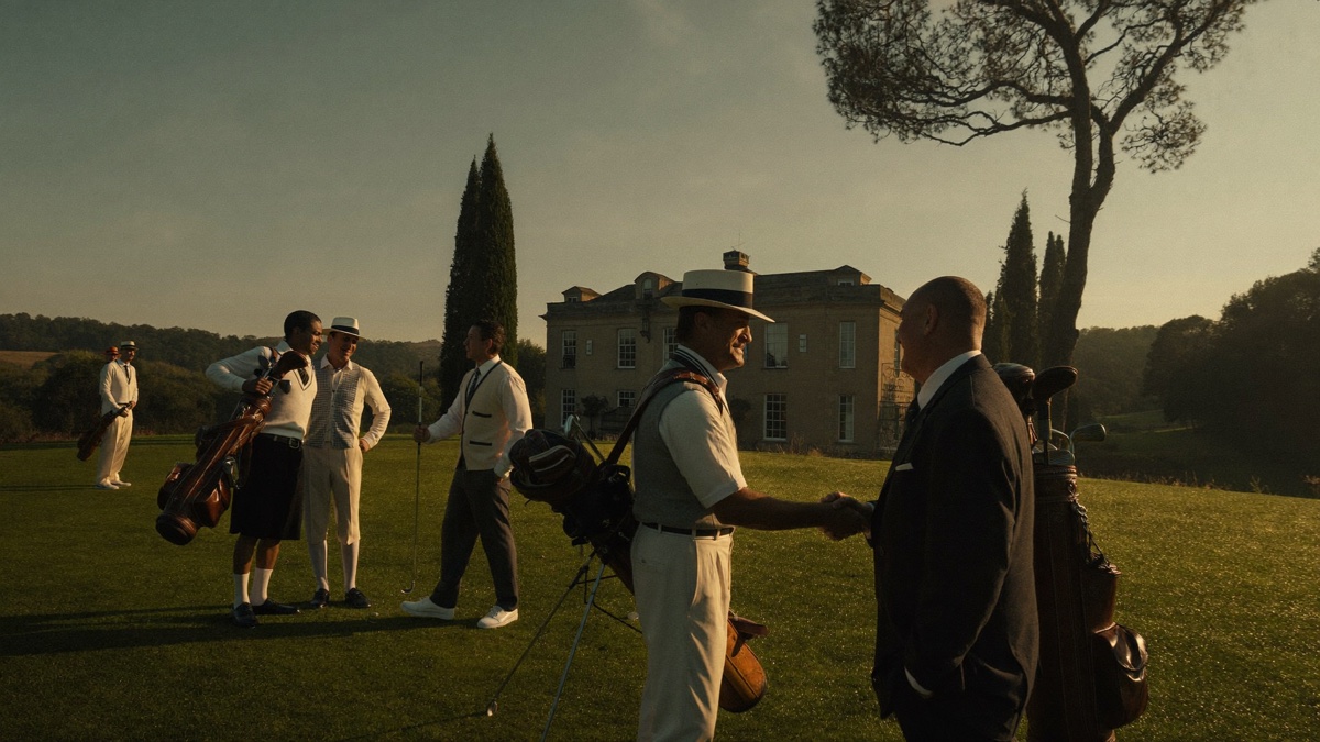 Golfers greeting each other with a handshake on the first tee of a classic country club at golden hour, leather golf bags over their shoulders