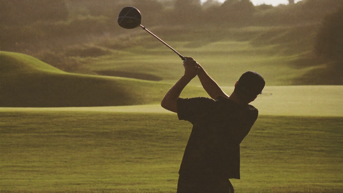 Golfer at the top of a controlled, compact driver swing at golden hour, wide fairway and links mounding beyond