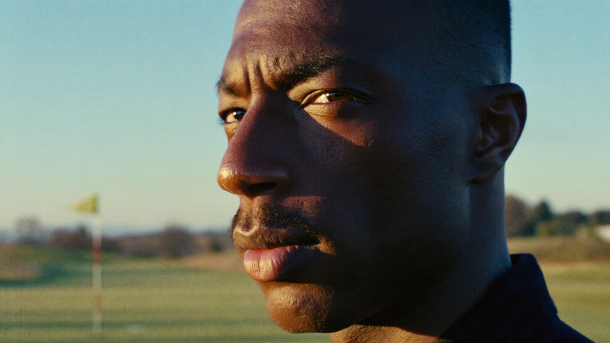 Close-up of a golfer's face at golden hour, eyes narrowed and locked on a distant flag, completely focused before the shot