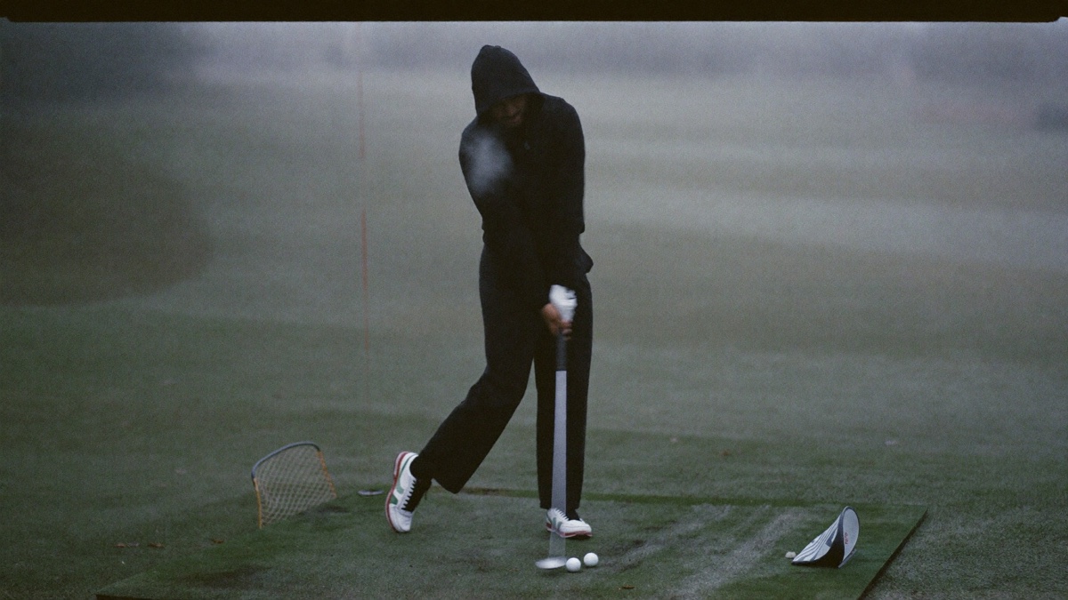 A dedicated golfer practicing alone on an empty driving range on a cold gray morning, breath visible in the chilly air, working with focus when no one is watching