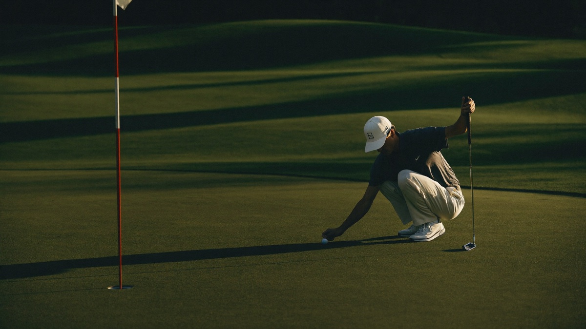 A golfer reading a putt on a green at golden hour