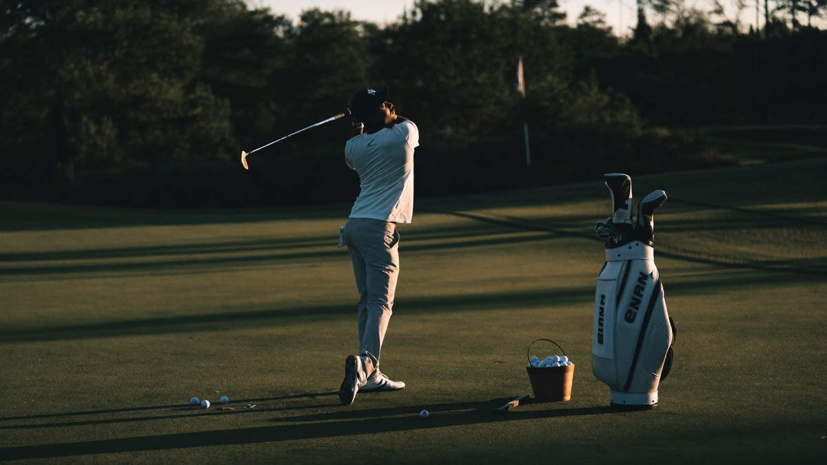 A golfer practicing driver on a range at golden hour